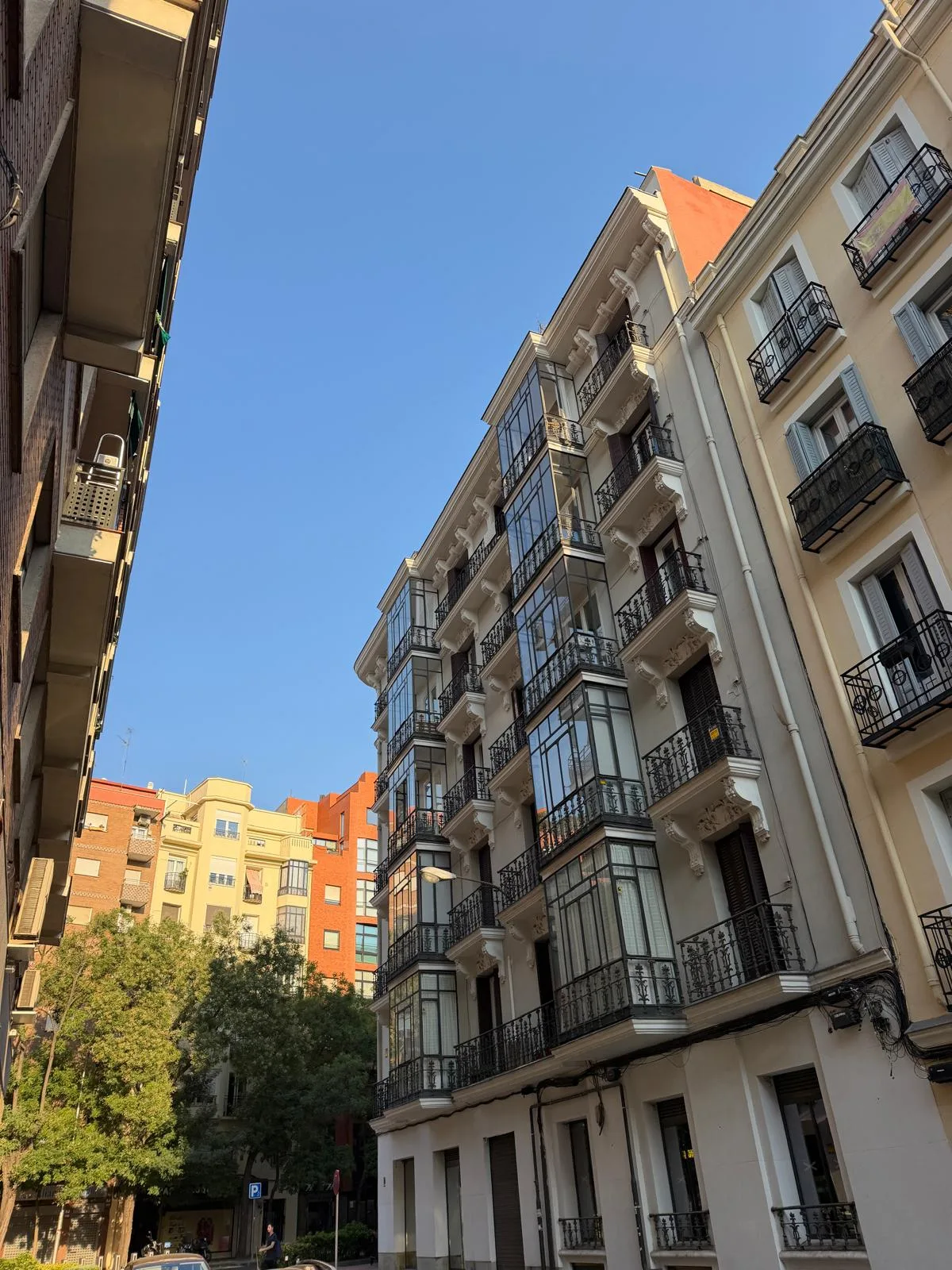 Calle residencial de Chamberí por la mañana, balcones con rejas de hierro, toldos, movimiento discreto de vecinos.